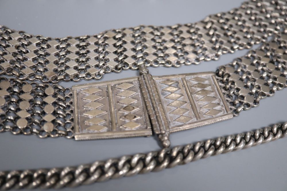 An Indian white metal belt and two alberts including silver and a silver and yellow metal medallion.